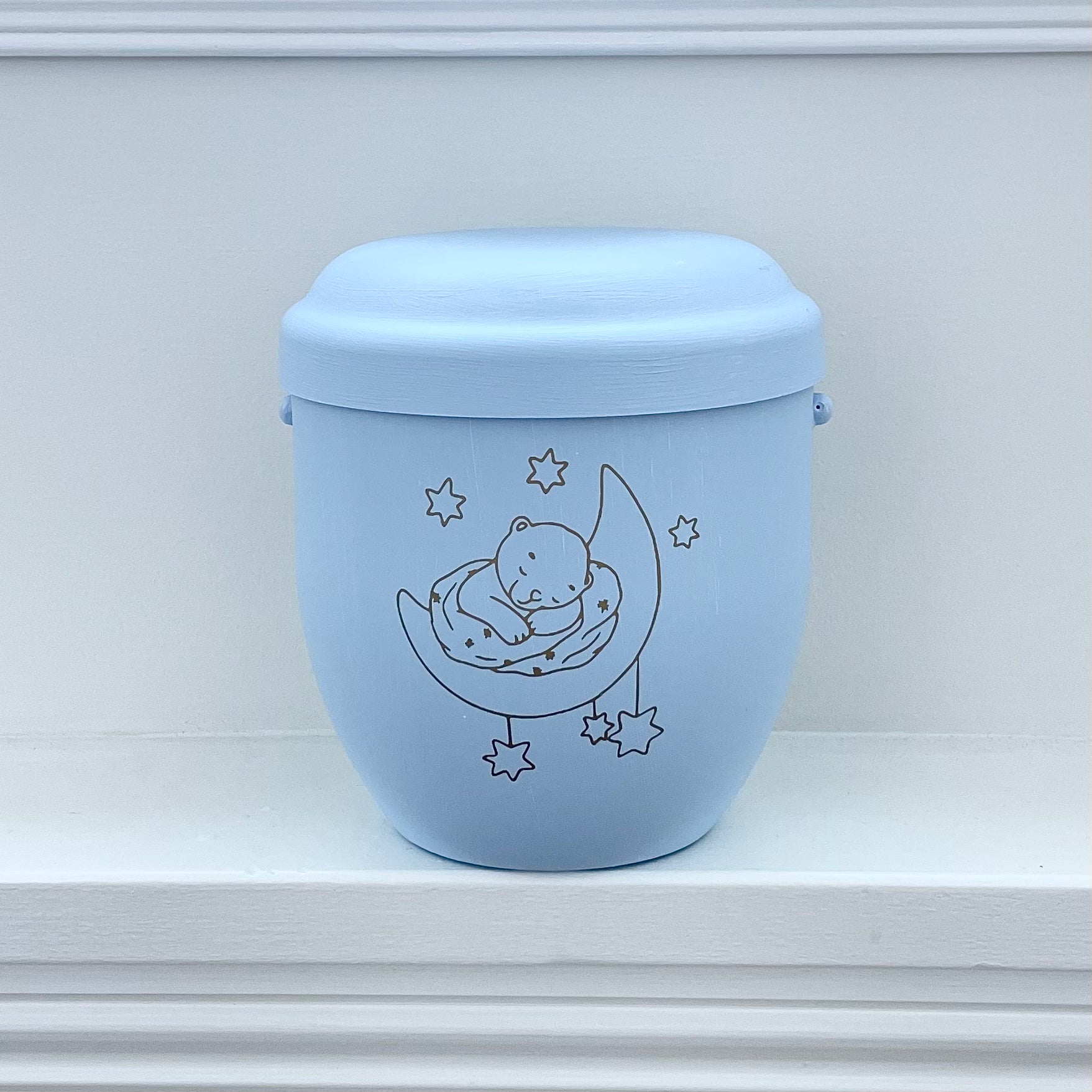 Beautiful light blue infant urn with a little Teddy Bear asleep on a half moon and surrounded by stars. Can be personalised with a name and dates or a few loving words.