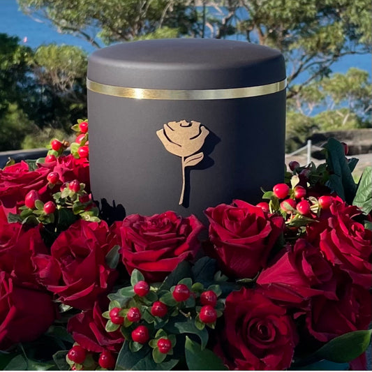 Elegant black funeral urn with a symbol of a golden rose set in a beautiful  wreath of red roses.