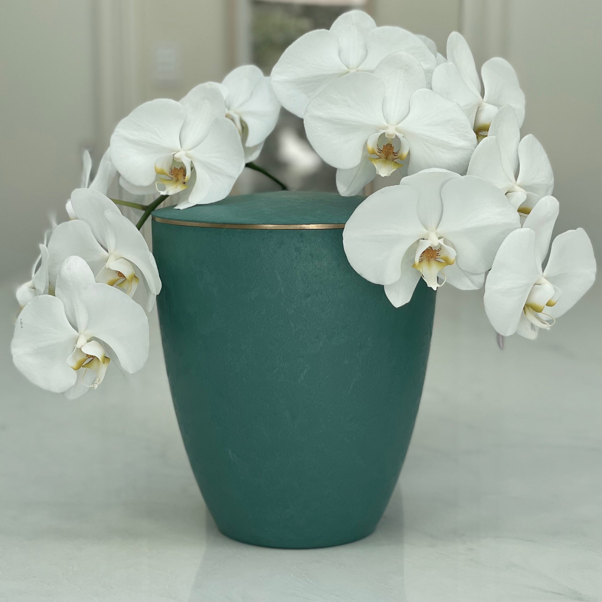 Elegant  emerald coloured urn for ashes with a delicate gold band with a flower arrangement of white orchids..