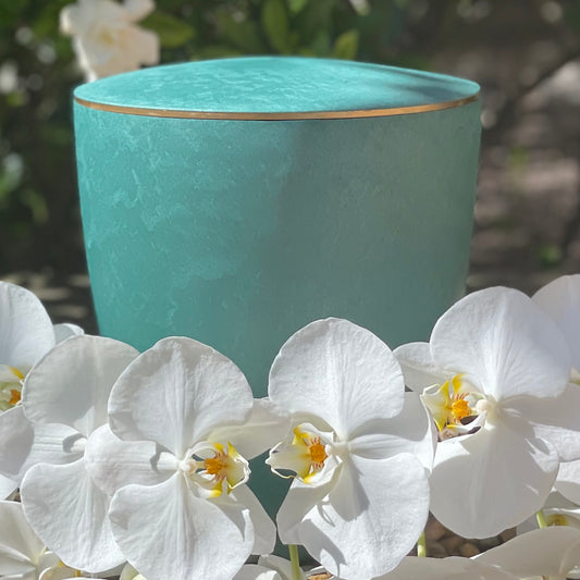 Beautiful emerald coloured urn for ashes with a delicate gold band with wreath of white orchids.