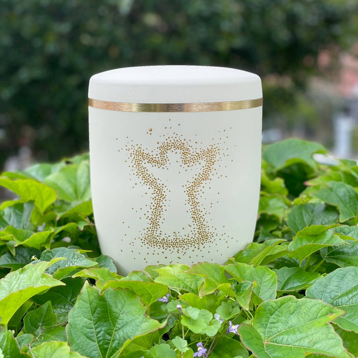 Beautiful ivory coloured cremation urn with the silhouette of an angel hand-pained with golden dots surrounded by green ivy.