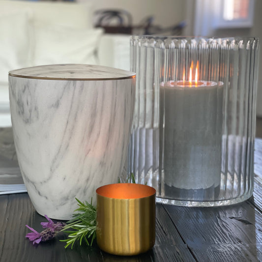 Stunning white marble imitation urn for ashes with a delicate gold band next to burning candles.