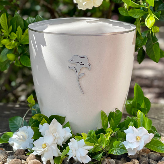 Stunning off-white coloured urn for ashes with a symbol of a silver lily set in a wreath of white flowers and foliage.