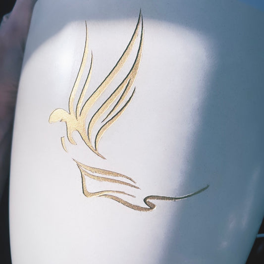 Close up of beautiful  hand-painted golden angel on off-white funeral urn.