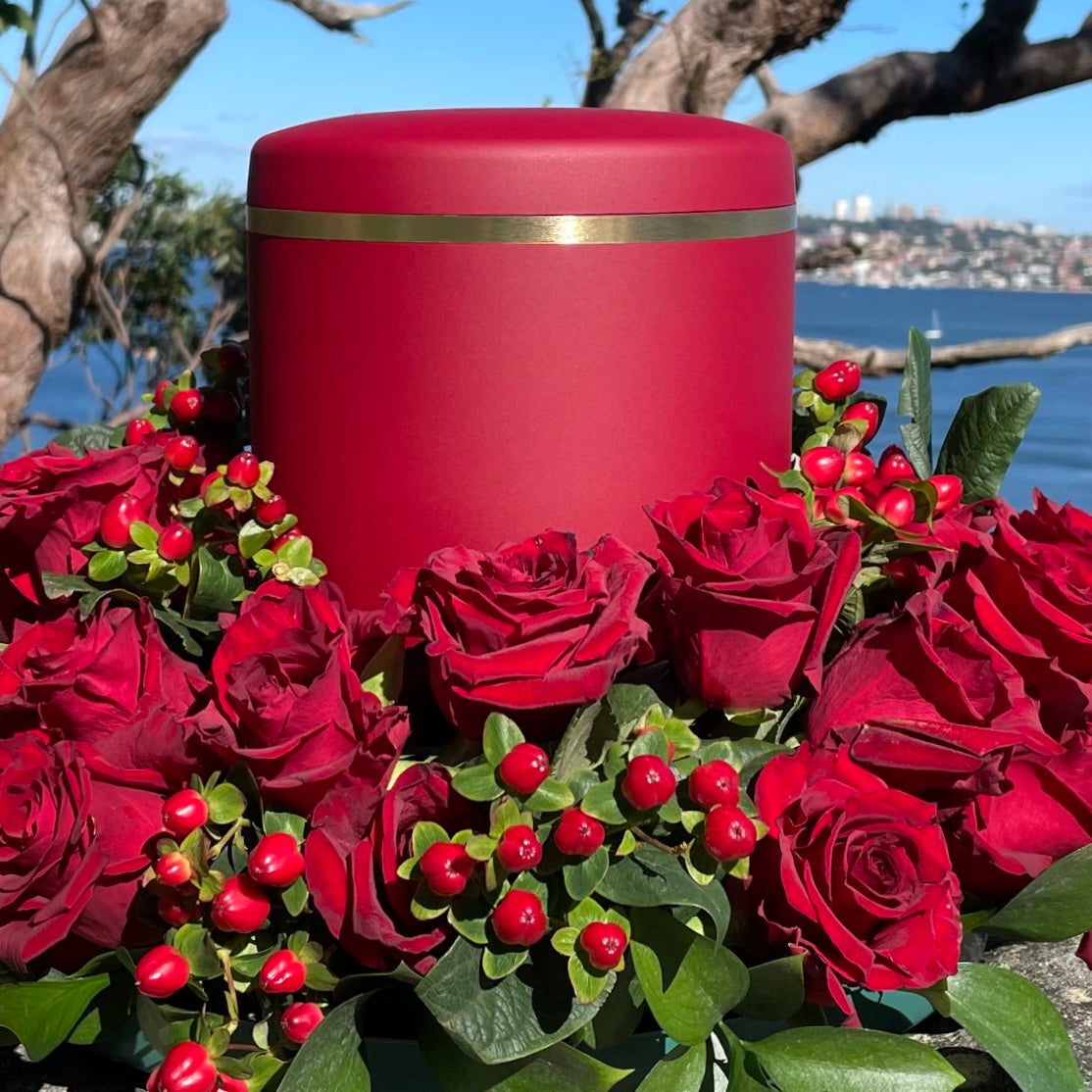 Elegant red cremation urn with a delicate brushed gold band in a wreath of red roses.