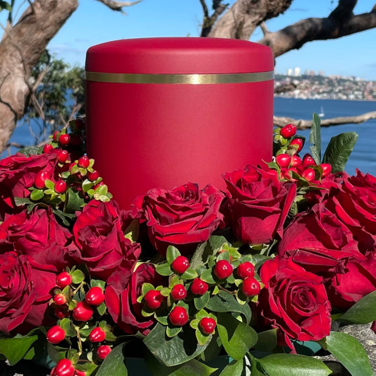 Elegant  red cremation  urn  with a delicate brushed gold band in a wreath of red  roses.