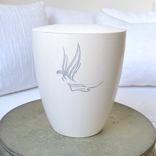 Beautiful off-white coloured funeral urn has been engraved with a guardian angel and hand-painted with liquid silver on a hammered silver table.