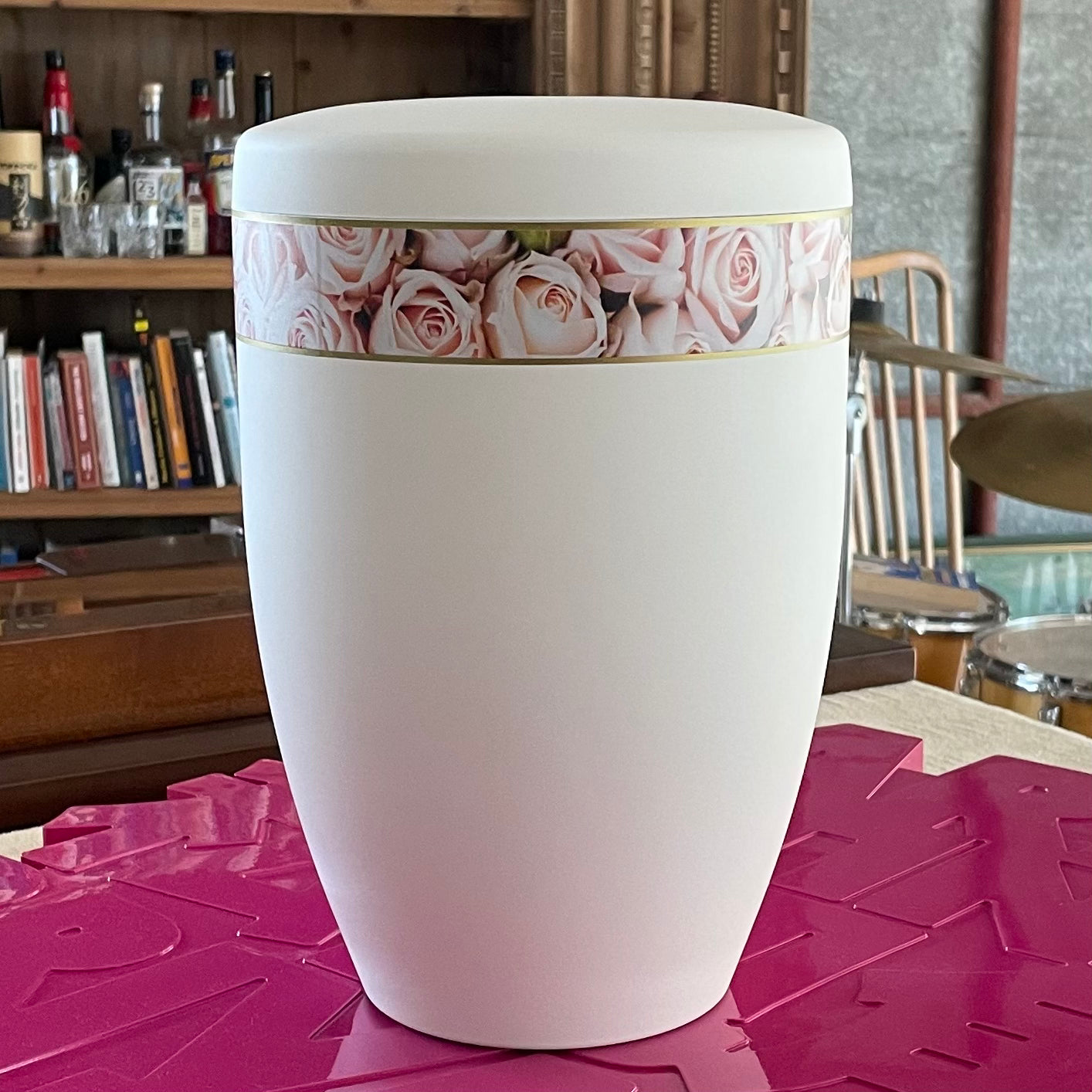 Beautiful white urn for ashes with its band of delicate pink roses sitting on pink artwork.