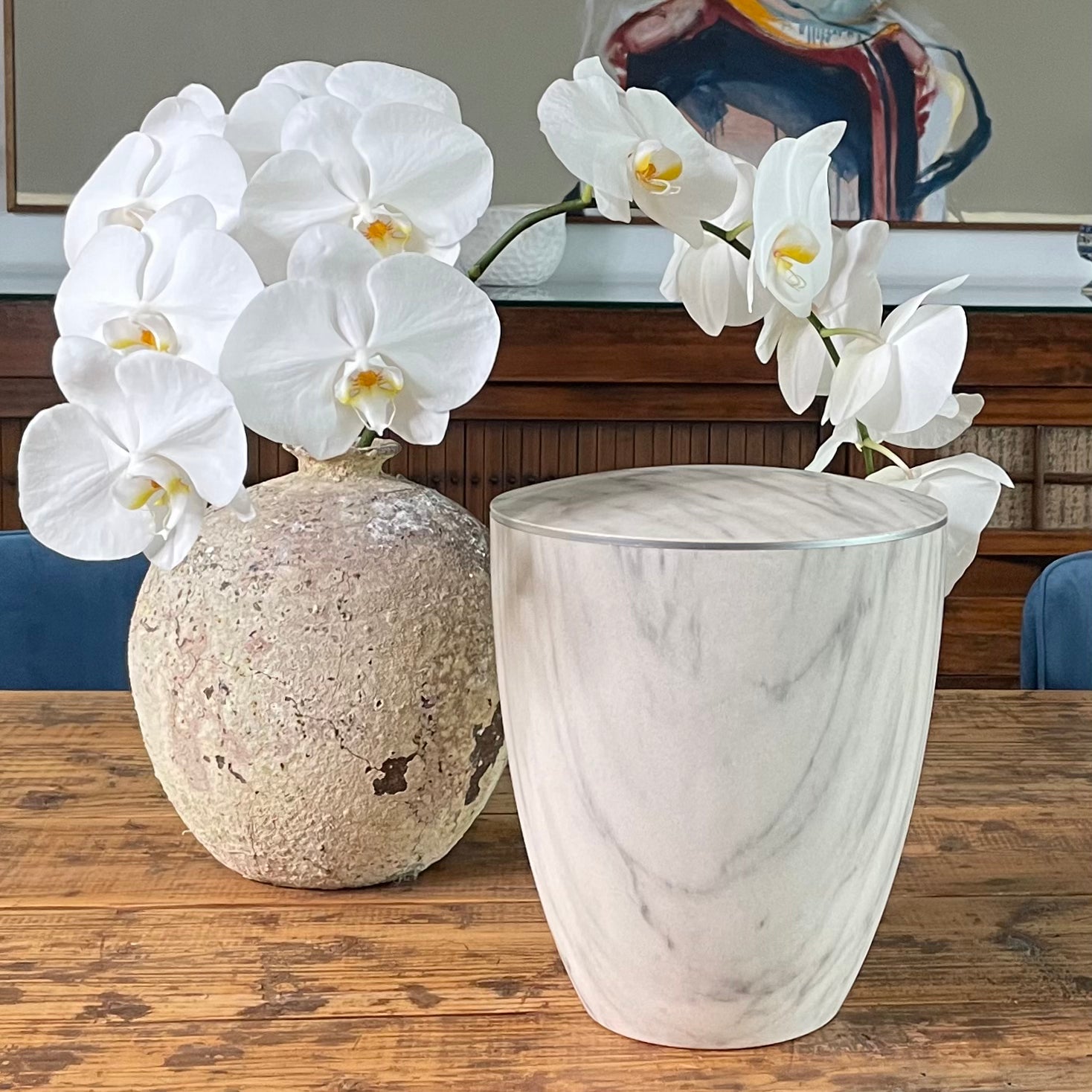 Stunning white marble imitation urn for ashes with a delicate silver band on antique table next to vase with orchids.